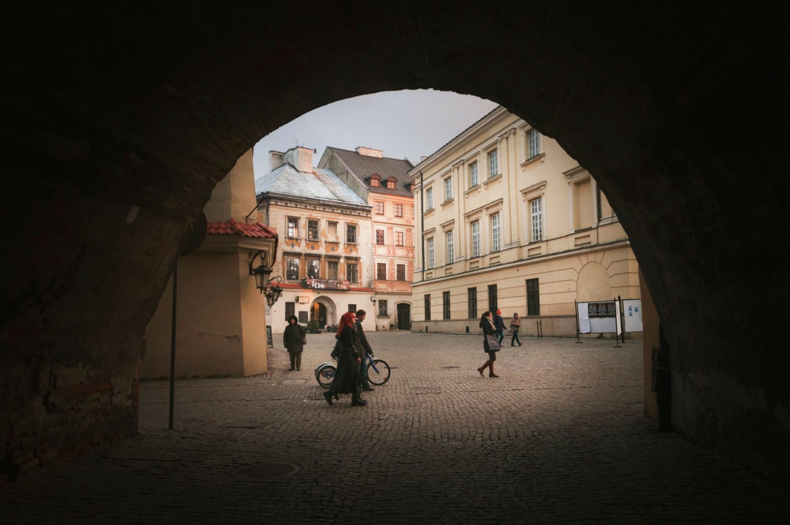 Home Through arched hole view of anonymous people strolling on tiled pavement between old urban house facades